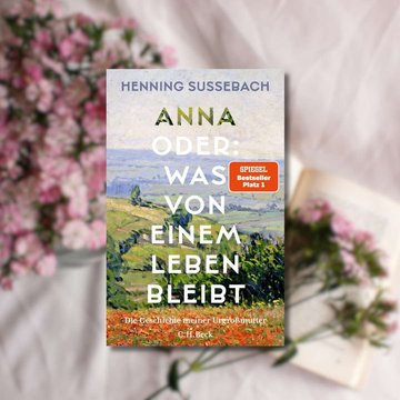 Buchtipp: „Anna oder: Was von einem Leben bleibt“ im Vordergrund. Im Hintergrund befinden sich ein weißes Laken sowie rosa Blumen.