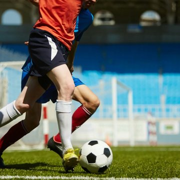 Zwei junge Männer spielen Fußball auf einem Rasen. Sie kicken einen schwarz-weißen Ball