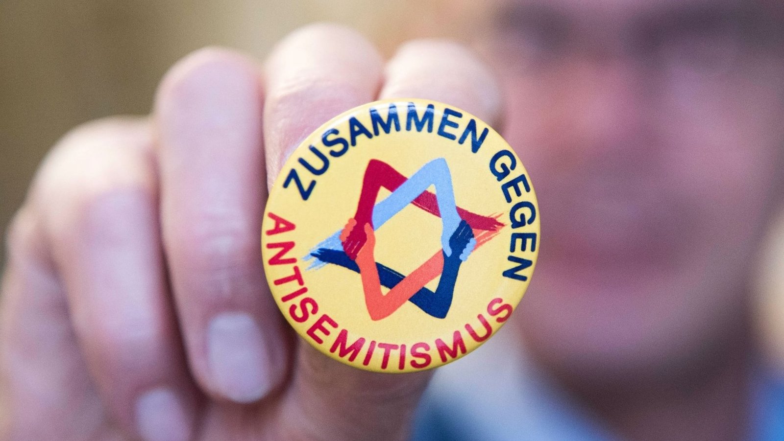 Auf dem Bild ist ein kleiner gelber Button zu sehen, auf dem ein bunter Davidstern zu sehen ist. Auf dem Button steht in Großbuchstaben: Zusammen gegen Antisemitismus.