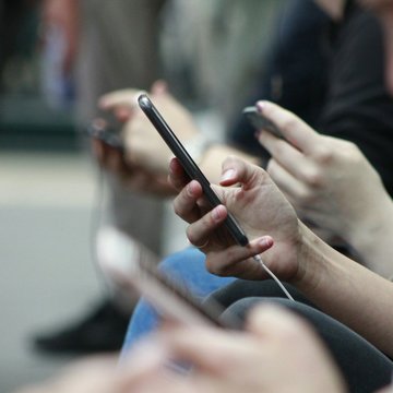 Eine Gruppe Menschen sitzt schräg hintereinander, alle halten ihr Handy in der Hand. 