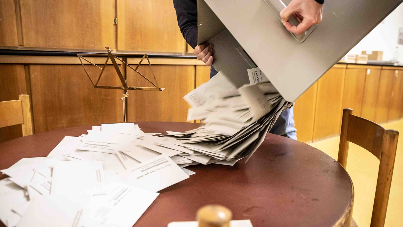 Zwei Personen schütten eine Box mit Wahlumschlägen auf einen Tisch.