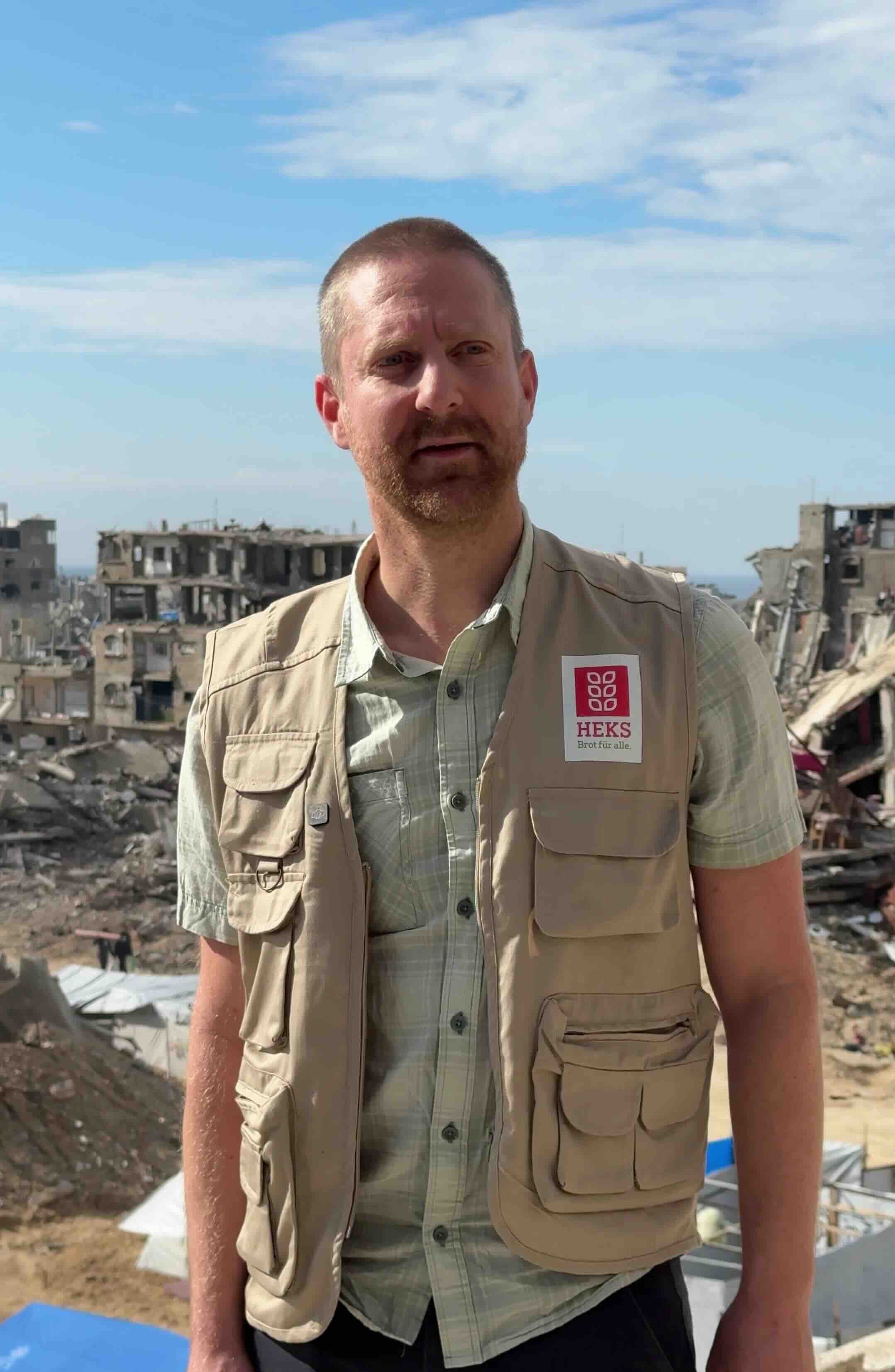 Porträtfoto von Sebastian Zug. Er trägt ein T-Shirt und eine beige Weste.