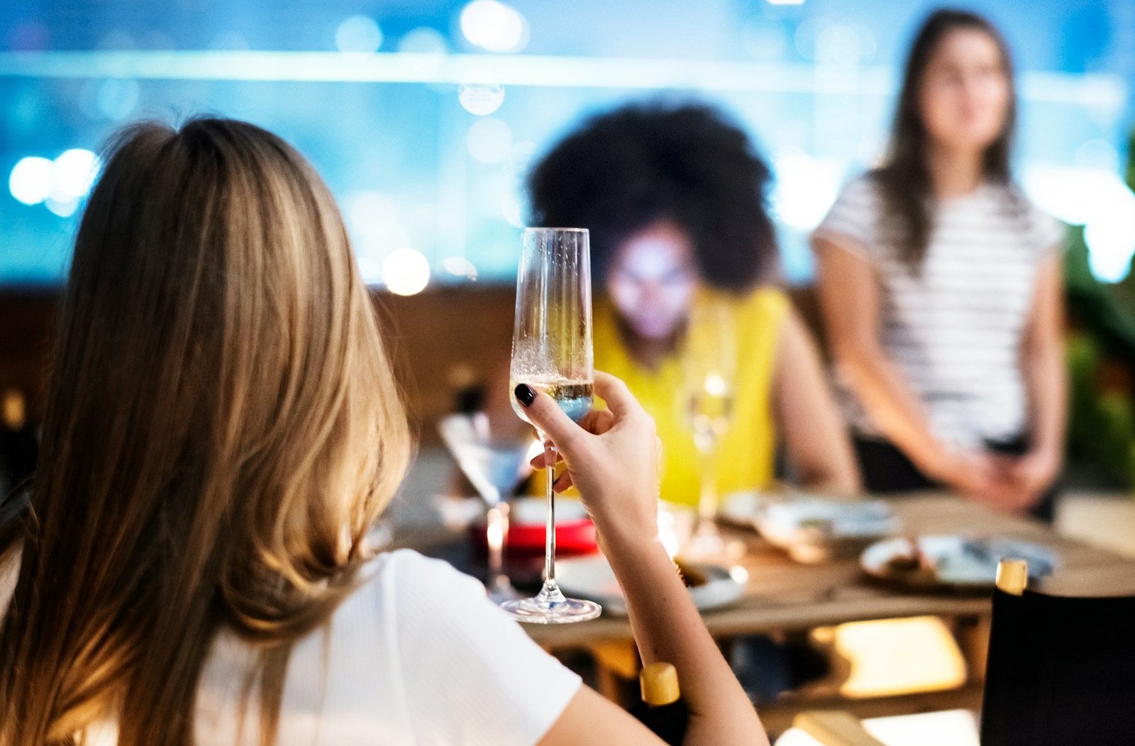 Eine Gruppe Frauen sitzt um einen Tisch. Eine Frau hat ein Sektglas in der Hand