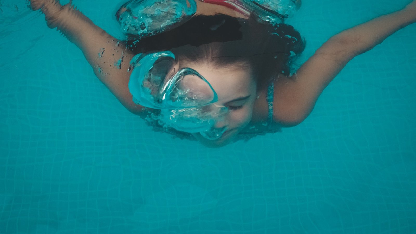 Ein Kind schwimmt unter Wasser, vor seinem Gesicht ist eine große Luftblase zu sehen.