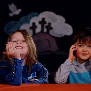 Ein Mädchen und ein Junge sitzen vor einem dunklen Hintergrund.