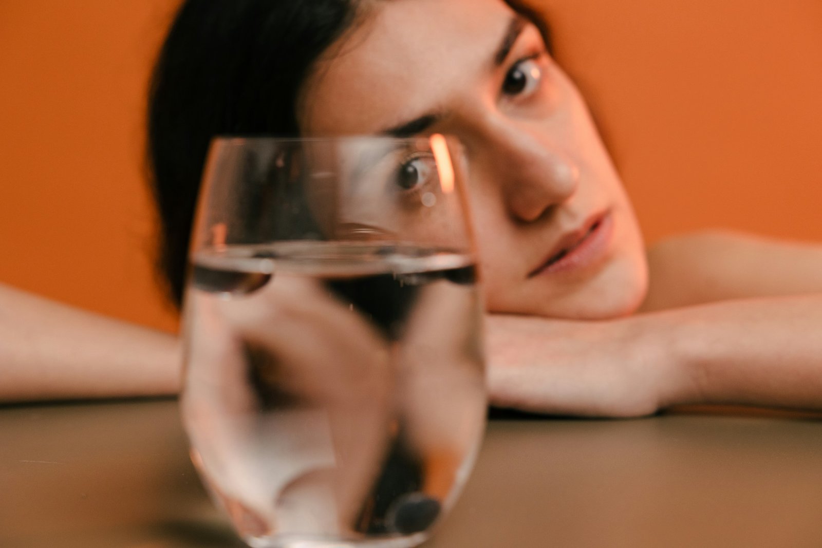Frau legt Kopf auf einen Tisch und blickt auf ein gefülltes Wasserglas