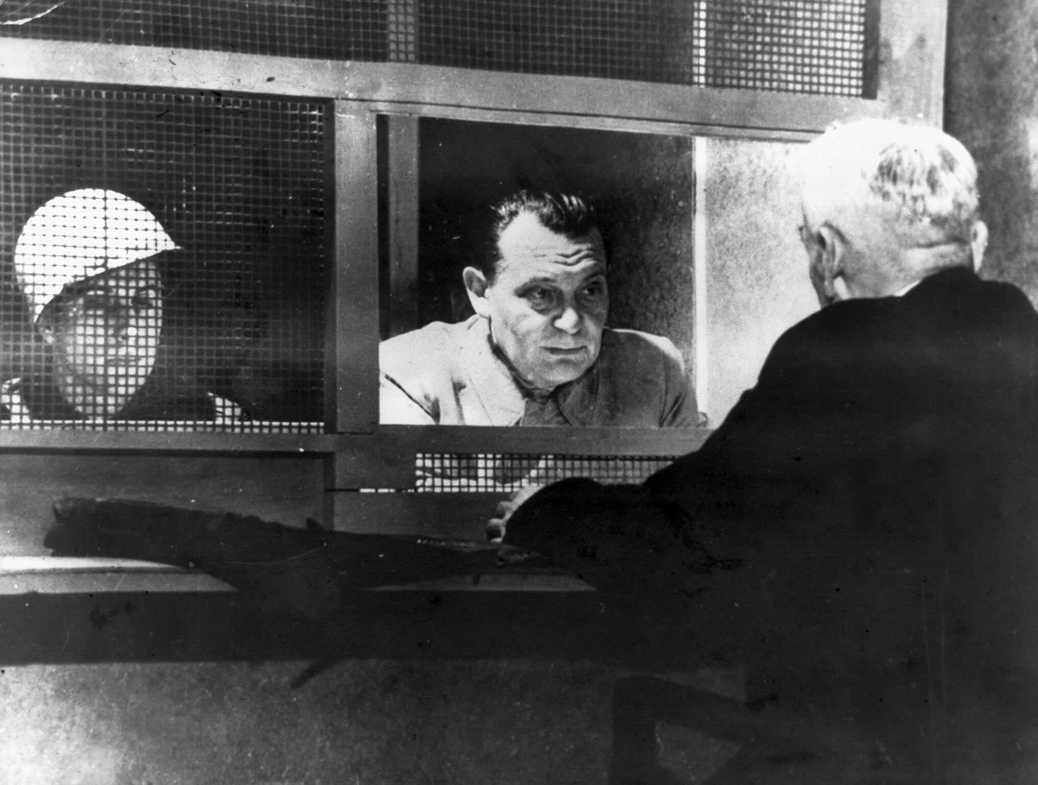 Eine schwarz-weiß Aufnahme von Hermann Göring im Nürnberger Gefängnis, sich mit seinem Anwalt Otto Stahmer beratend, der von hinten zu sehen ist.