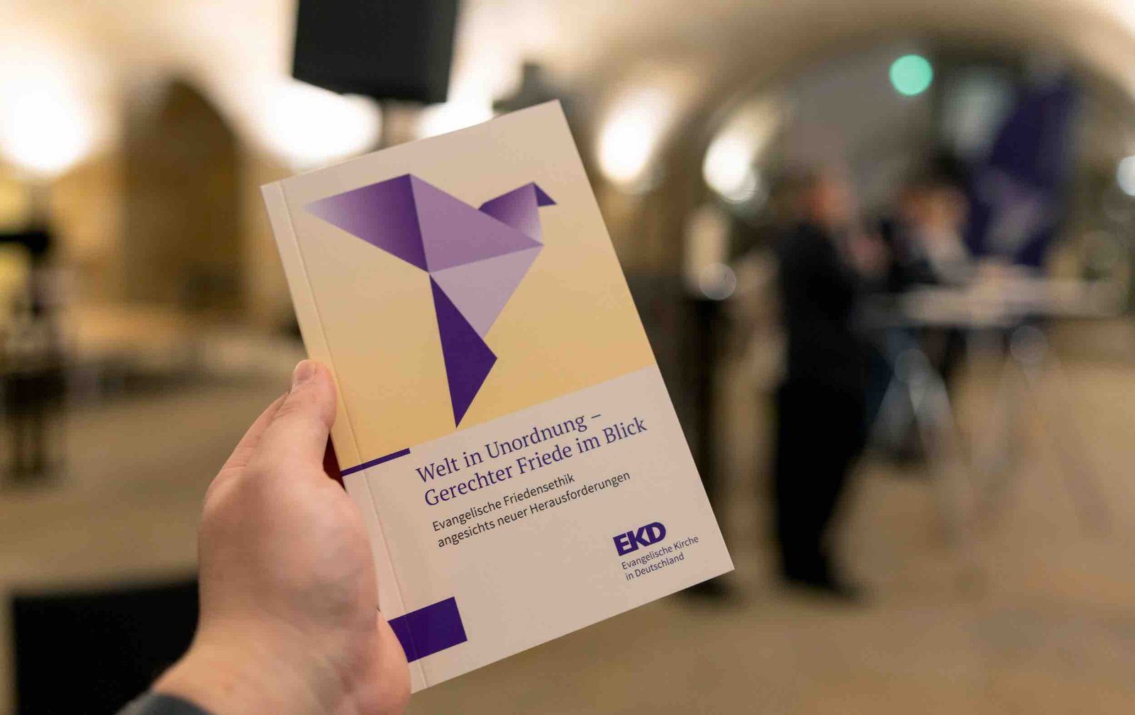 Eine Hand hält die Friedensdenkschrift der EKD mit dem Titel "Welt in Unordnung - Gerechter Friede im Blick"