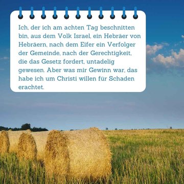Im Vordergrund steht der Bibelspruch. Im Hintergrund befinden sich drei Heuballen auf einer grünen Wiese. Der Himmel ist strahlend blau mit einigen Wolken.