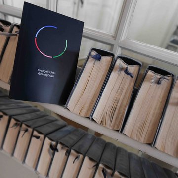Das neue evangelische Gesangbuch ist aufgestellt ein einem Regal mit anderen Büchern.
