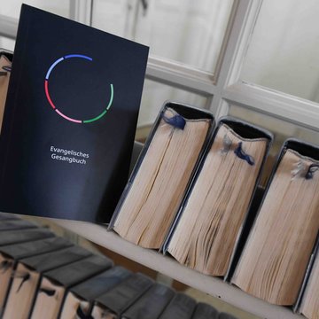 Das neue evangelische Gesangbuch ist aufgestellt ein einem Regal mit anderen Büchern.