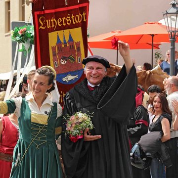 Reinszenierung der Hochzeit Martin Luthers und Katharina von Boras. Eine Frau (in grünem Kleid) und ein Mann (in schwarzer Mönchskutte) laufen durch eine Menschenmasse.