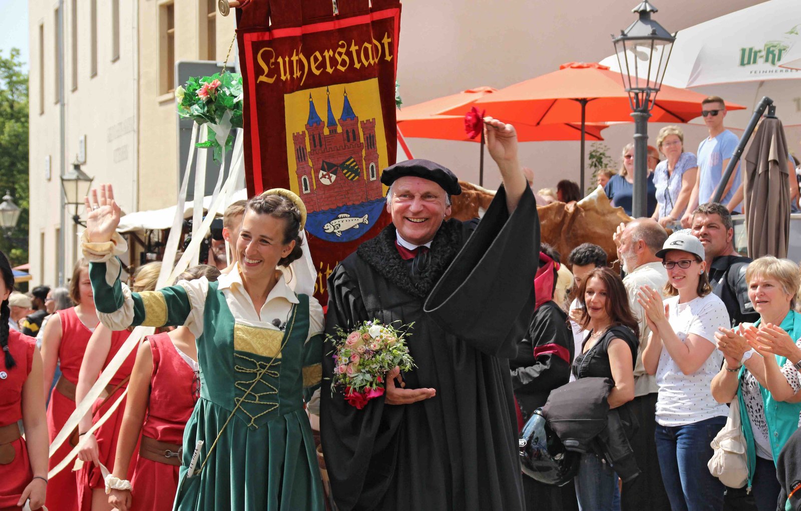 Reinszenierung der Hochzeit Martin Luthers und Katharina von Boras. Eine Frau (in grünem Kleid) und ein Mann (in schwarzer Mönchskutte) laufen durch eine Menschenmasse.