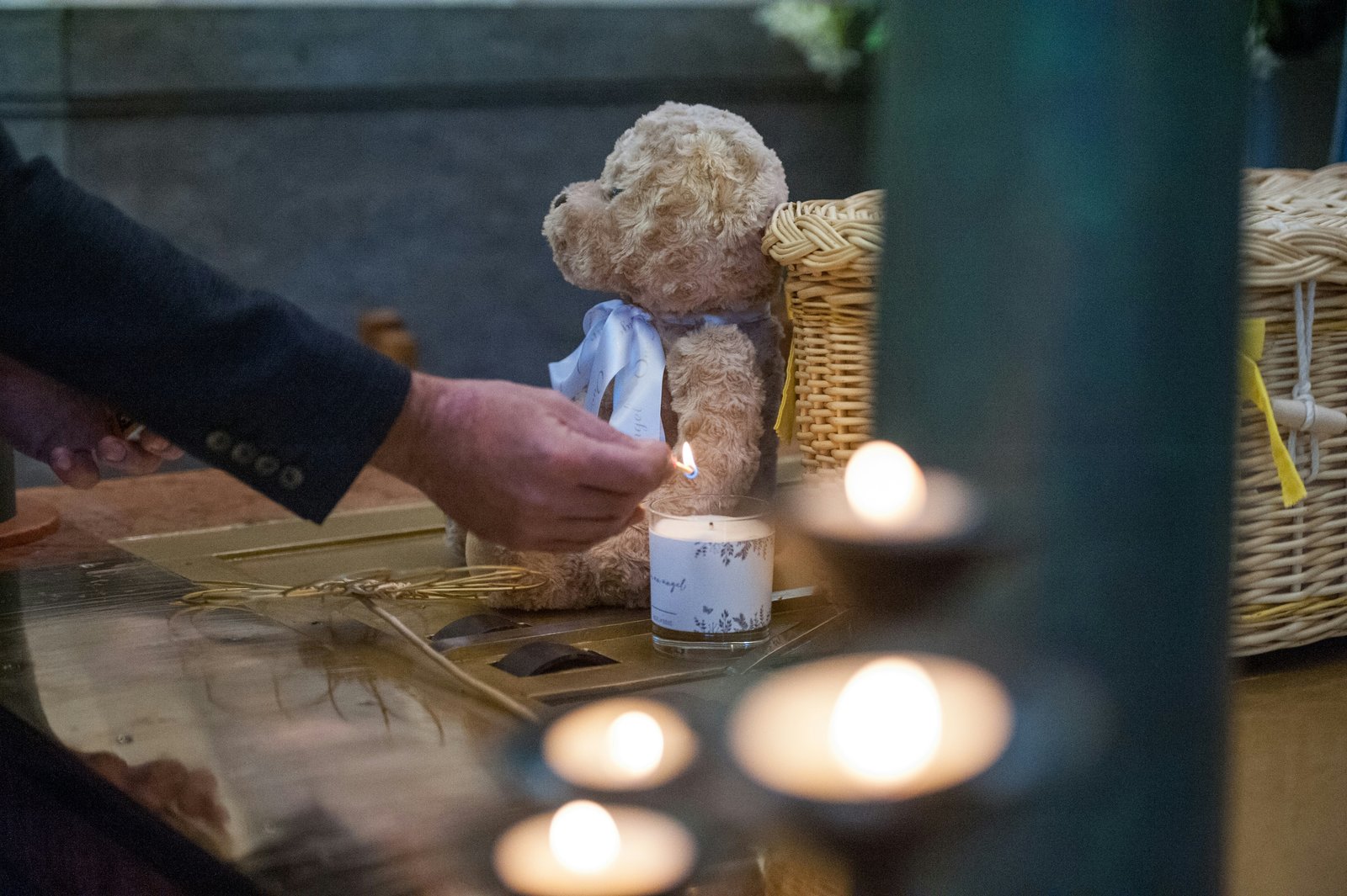 Mensch zündet eine Kerze an, daneben sitzt ein Teddybär auf dem Boden und weitere Kerzen.