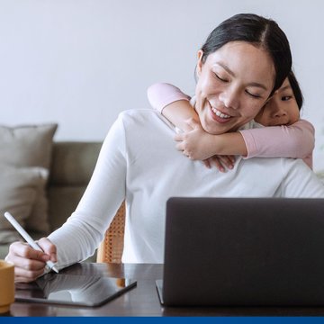 Eine junge Frau wird bei der Arbeit im Home Office von ihrer Tochter umarmt.