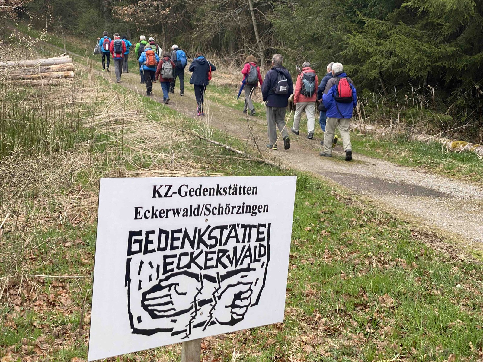 Im Vordergrund eine Tafel auf der Gedenkstätte steht, rechts daneben ein Weg auf dem Wanderer laufen.