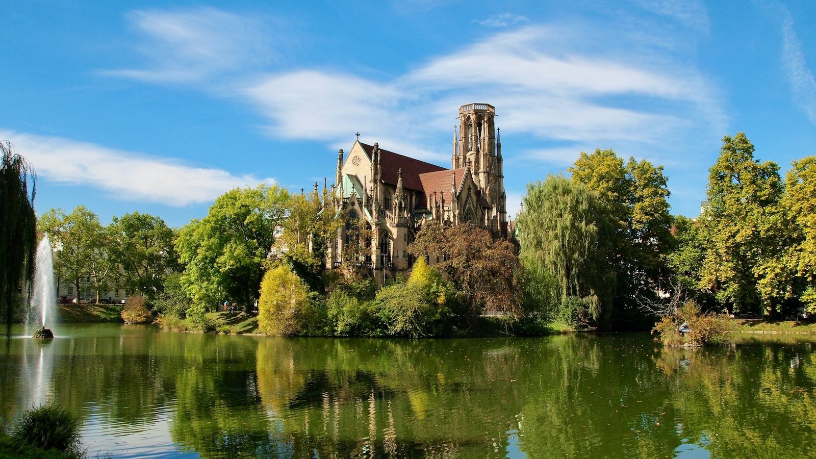 Die Johannes Kirche in Stuttgart ist auf dem Foto zu sehen. Sie liegt am Feuersee und ist umgeben von grünen Bäumen.