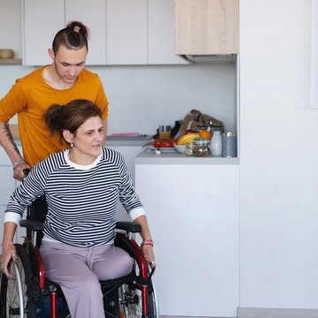 Ein junger Mann schiebt eine Frau im Rollstuhl. Die Frau ist an einem Bein über dem Knie amputiert.