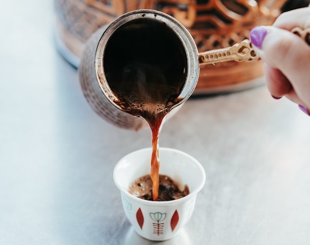 Eine Person gießt Kaffee aus einem Kännchen in eine kleine Tasse