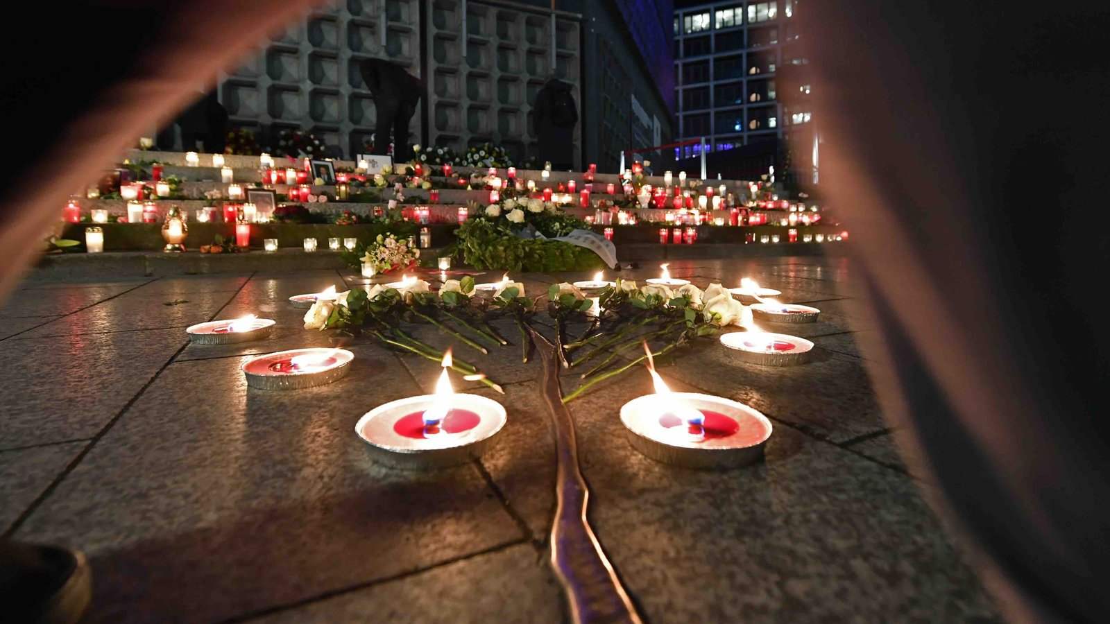  Das Bild zeigt den Berliner Breitscheidplatz bei Dunkelheit: Auf dem Boden stehen angezündete Teelichter und andere Kerzen. Außerdem sind Rosen niedergelegt. Auf dem Boden ist eine Linie aus goldfarbenem Metall zu sehen.