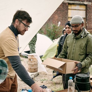 Ein junger Mann/Freiwilliger mit dunklem Bart gibt Essen an Bedürftige aus 