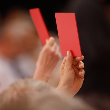 Rote Abstimmungskarten werden in der Hand gehalten.