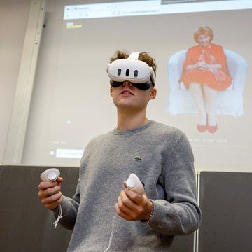 Junger Mann mit Virtual-Reality Brille, im Hintergrund ist ein großes Bild von Charlotte Knobloch zu sehen.