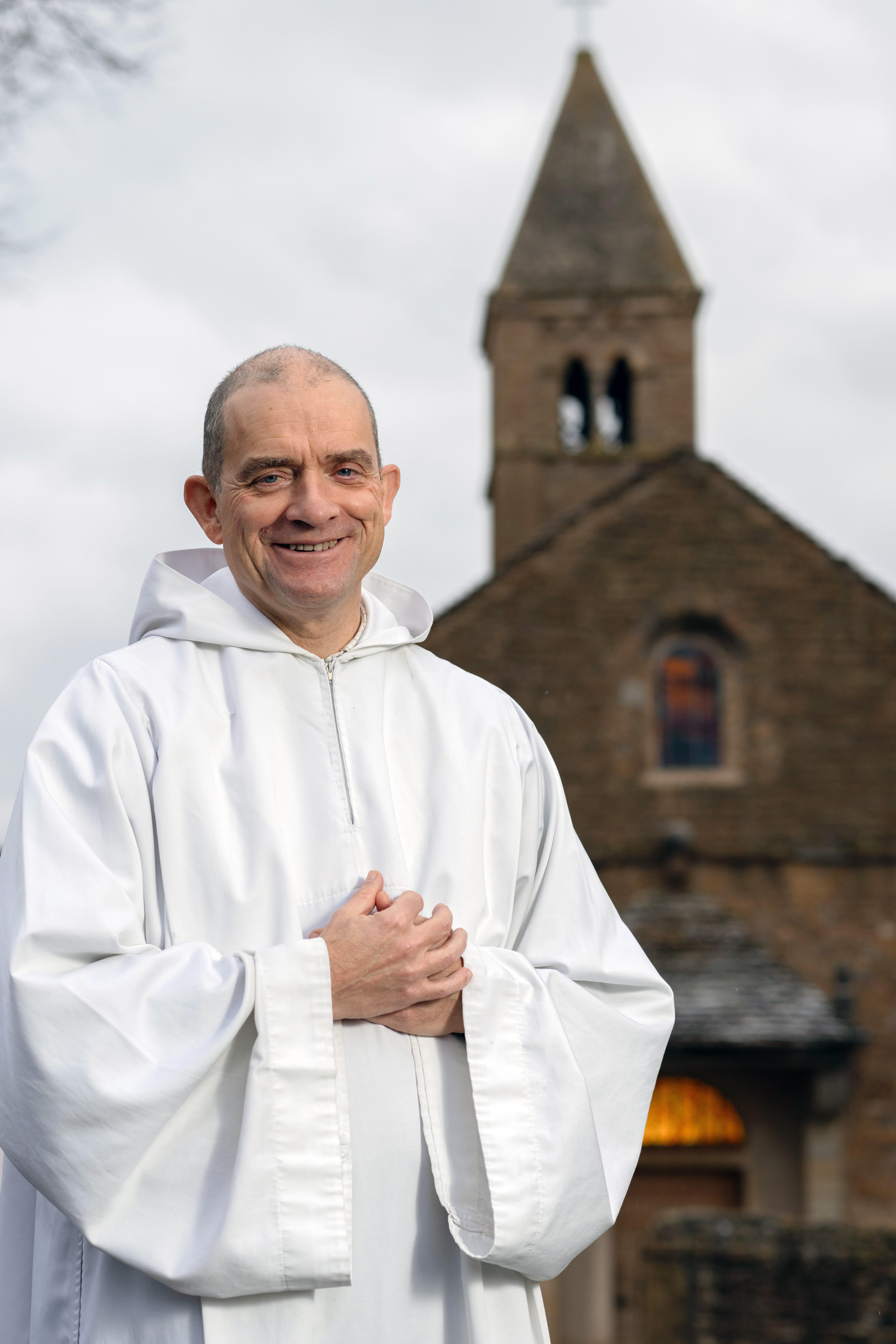 Frère Matthew steht im weißen Gewand vor einer Kirche.
