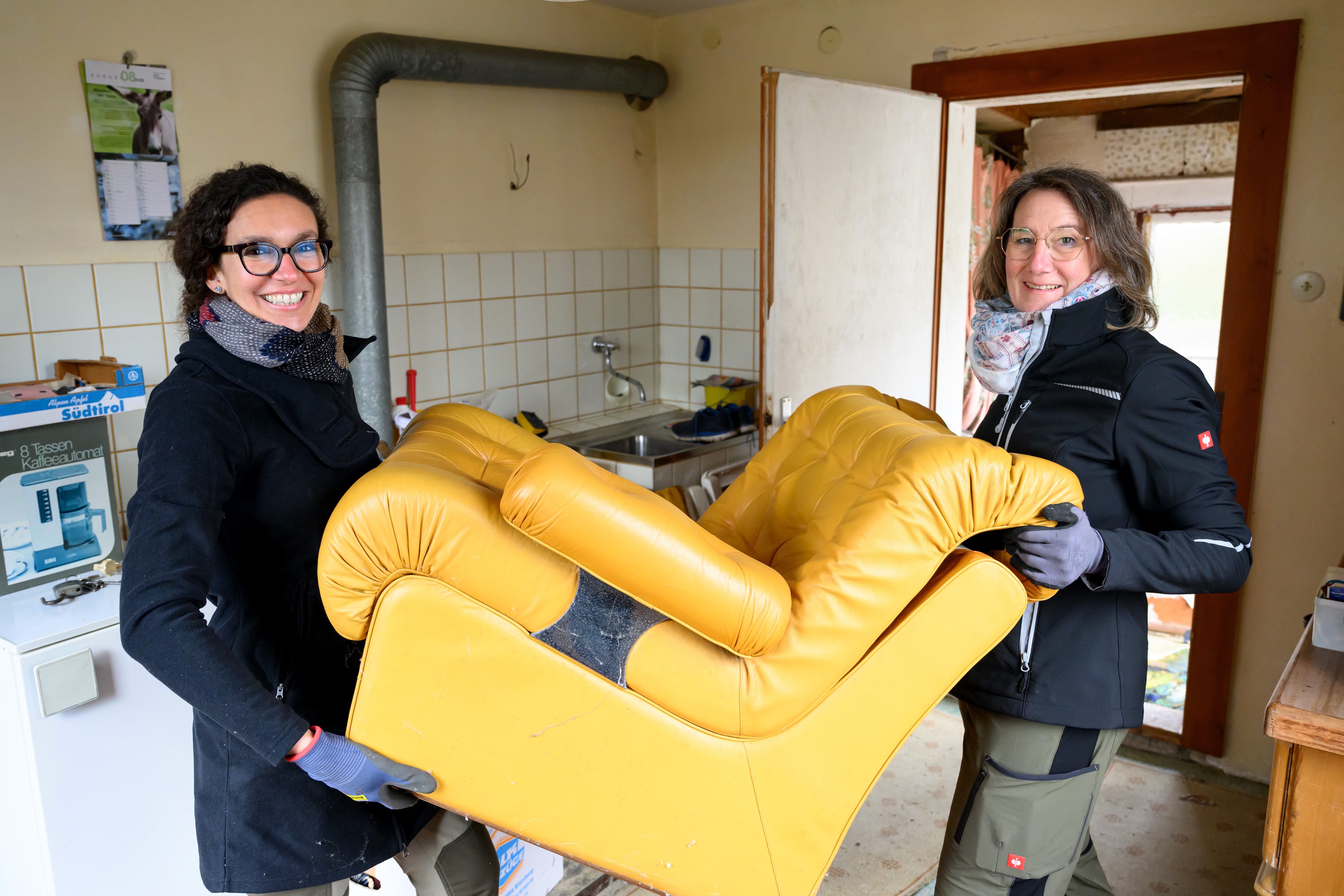 Zwei Frauen tragen ein gelbes Sofa.