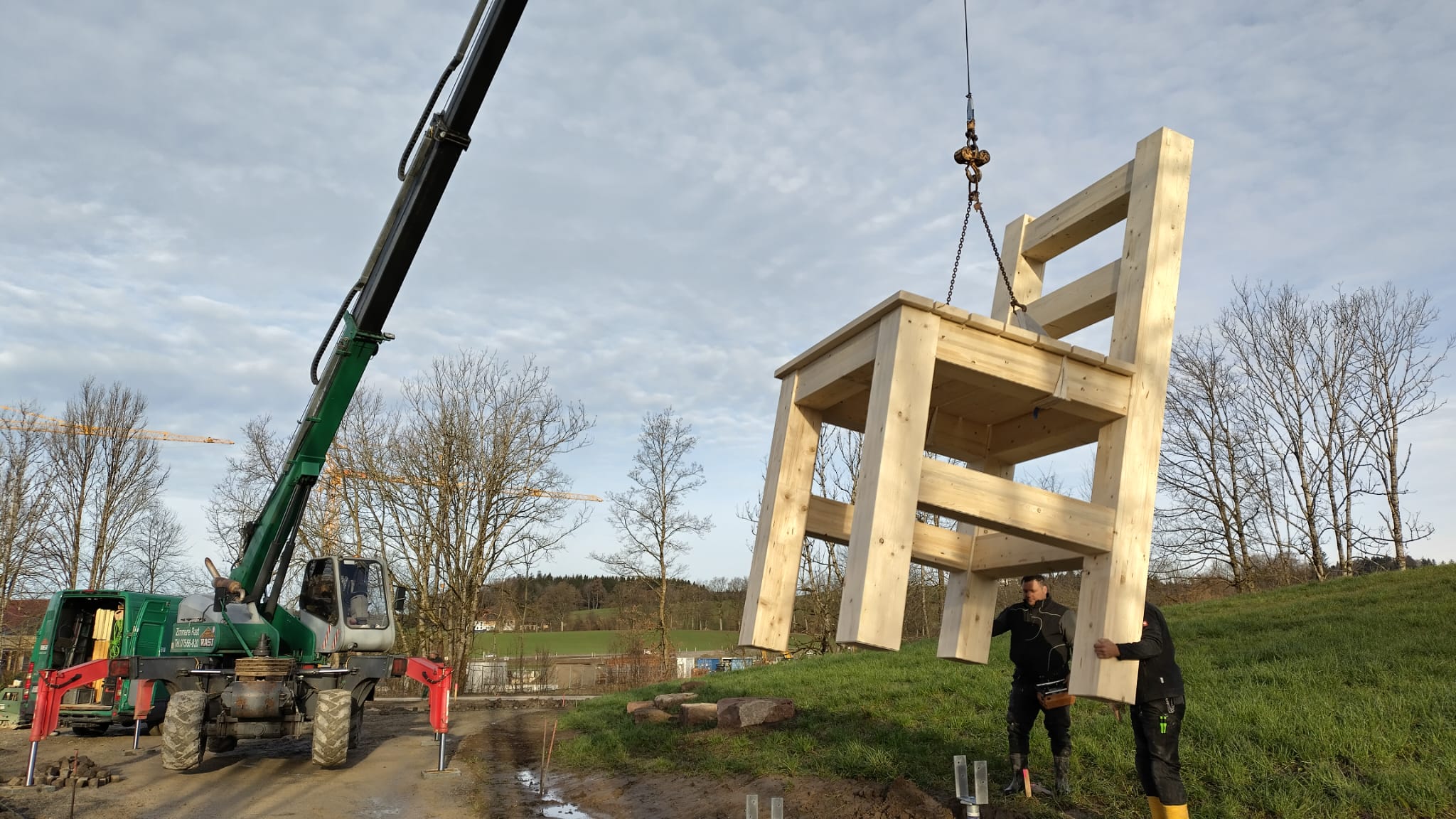 Ein überdimensional großer Holzstuhl hängt an einem Krahn.