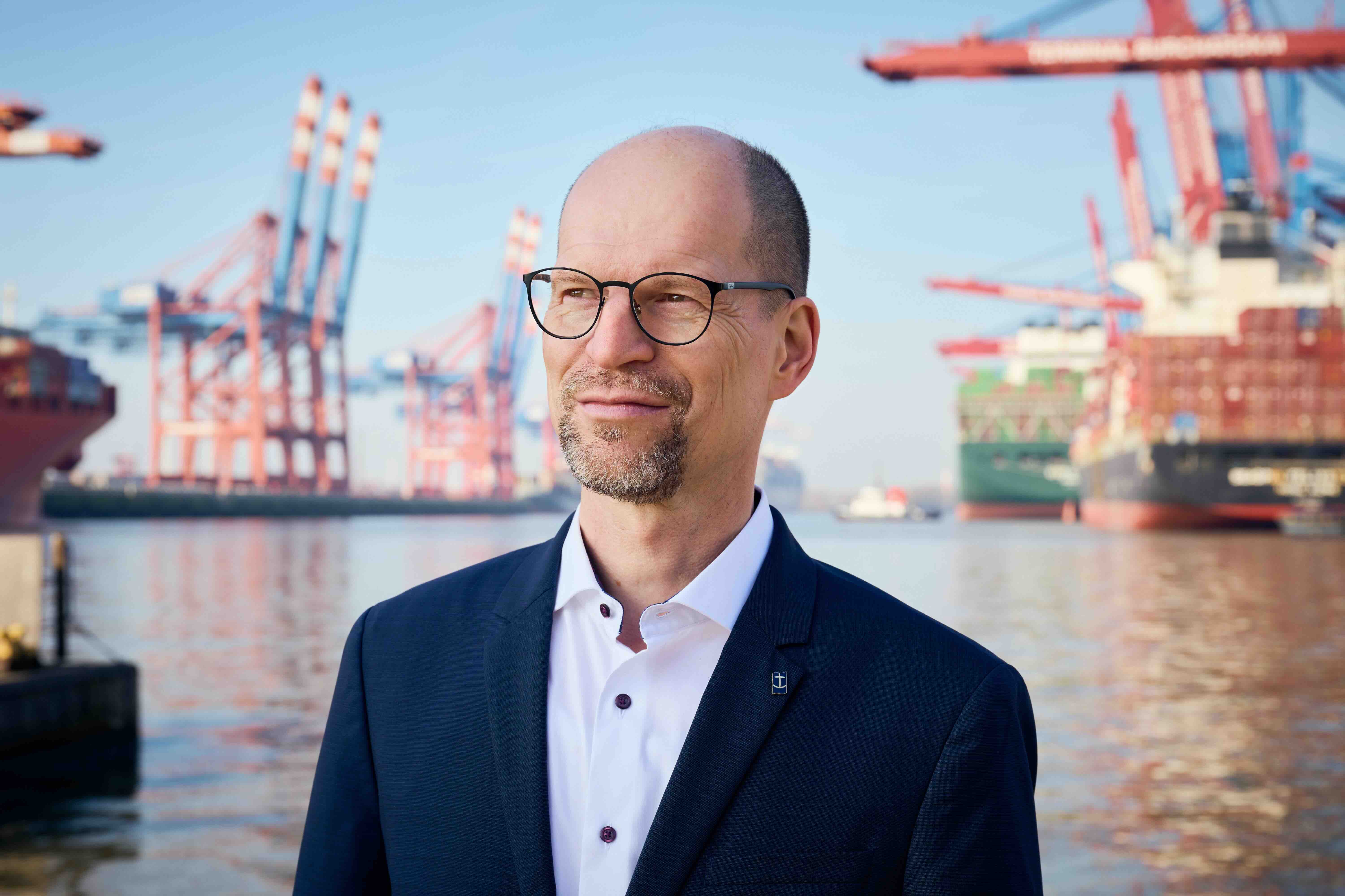 Das Foto zeigt Matthias Ristau, Generalsekretär der Deutschen Seemannsmission. Der Mann steht vor einem Containerschiff-Hafen.