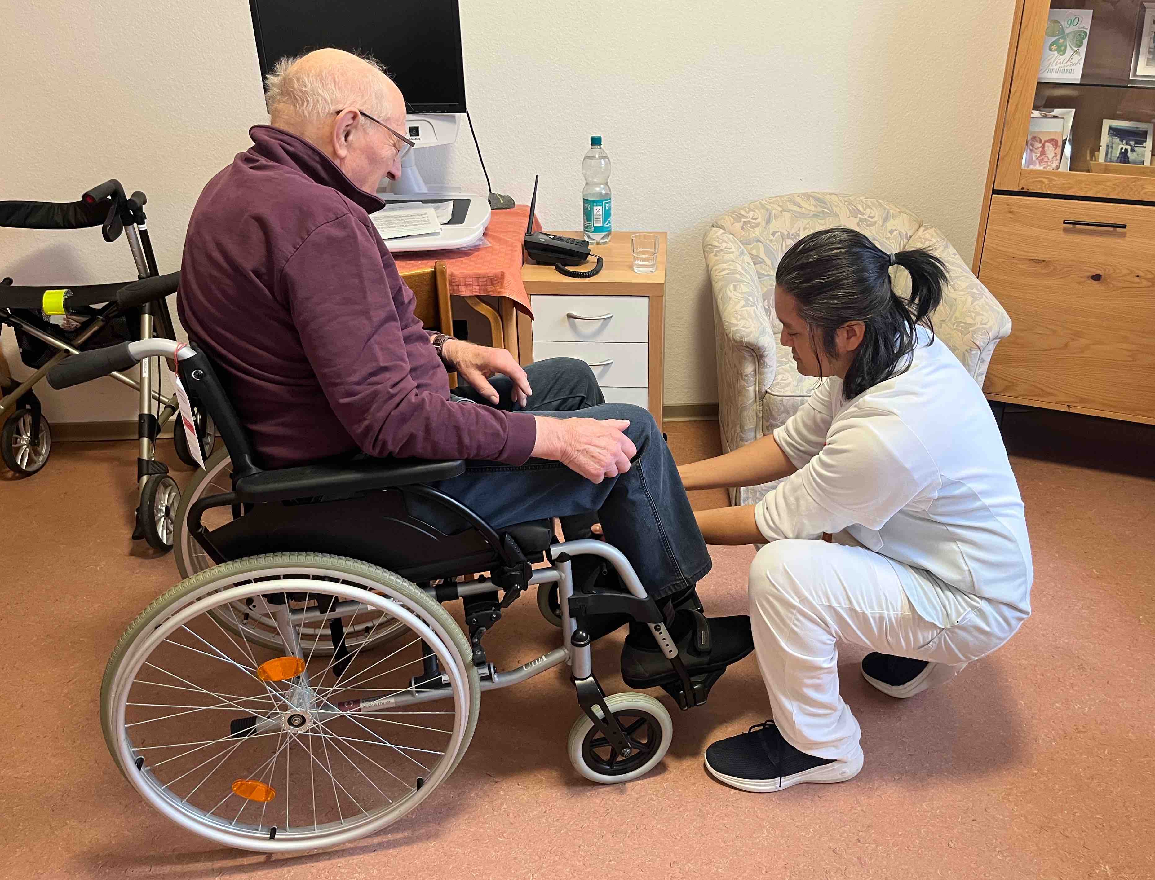 John Donasco bei der Arbeit als Altenpfleger mit einem älteren Herren, der im Rollstuhl sitzt