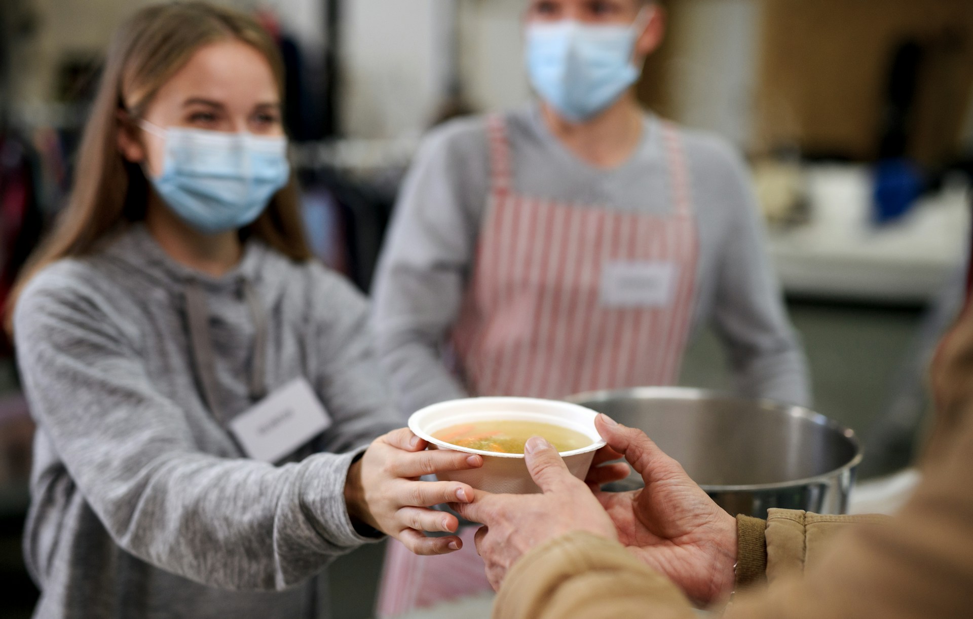 Junge Frau gibt einer Person eine Schüssel mit Suppe.