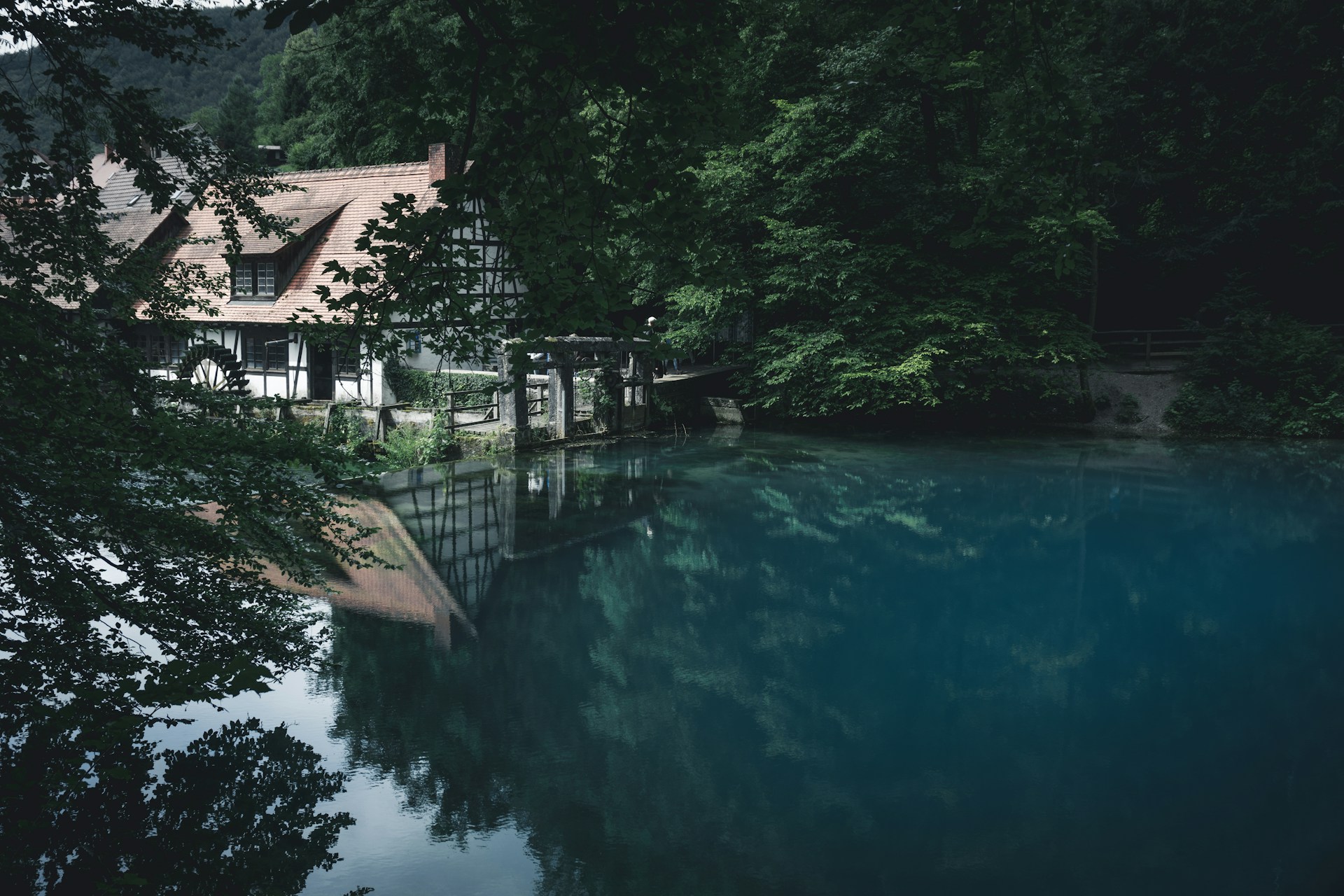 Aufnahme vom Blautopf in Blaubeuren: Ein weißes Fachwerkhaus mit dunklen Balken steht an einem Blauen See