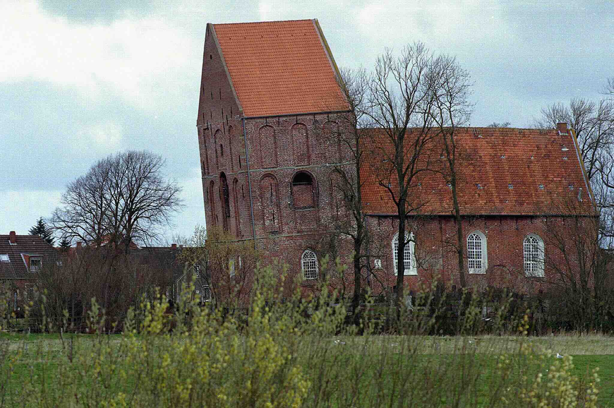 Die Dorfkirche von Suurhusen: Ein schiefer Kirchturm einer kleinen Backsteinkirche 